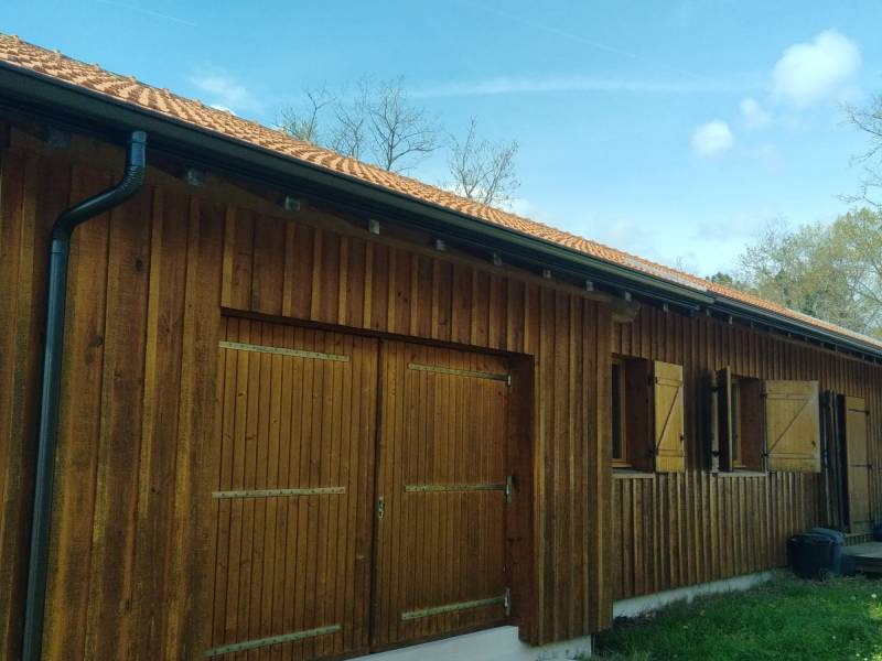 Installer des gouttières et leurs descentes noires graphite sur un gîte en bois à Moustey