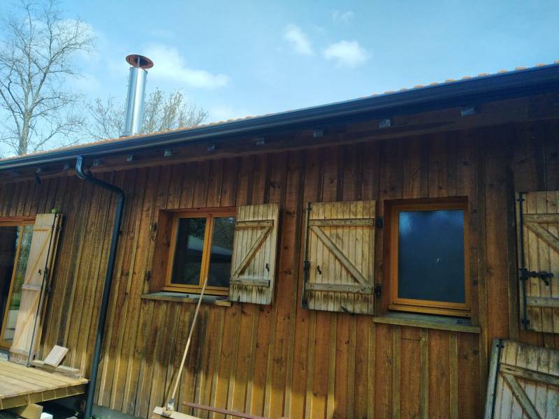 Comment installer des gouttières et leurs descentes noires graphite sur un gîte en bois à Moustey