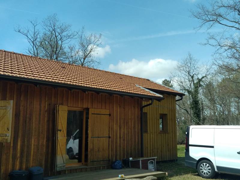 Faire installer des gouttières et leurs descentes noires graphite sur un gîte en bois à Moustey